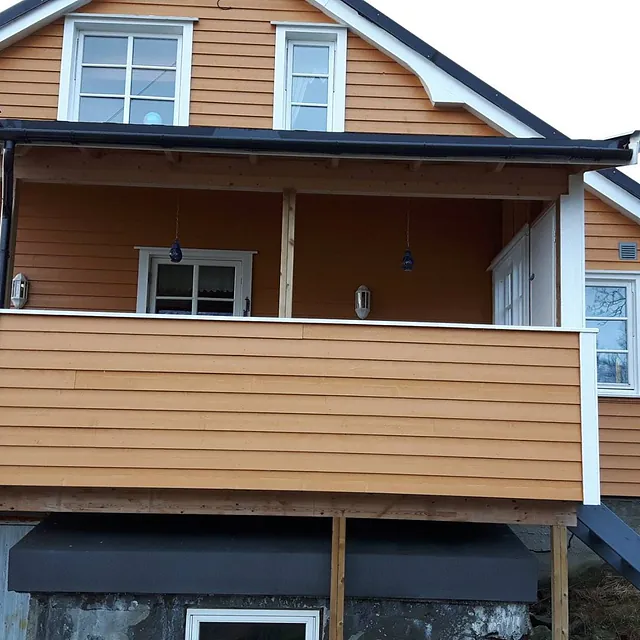 Et hus med en balkong som har gelender som matcher huset og tak over balkongen samt mange vinduer og dører med hvite karmer