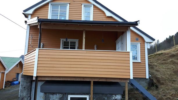 Et hus med en balkong som har gelender som matcher huset og tak over balkongen samt mange vinduer og dører med hvite karmer