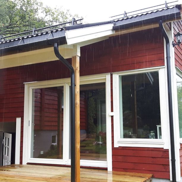 En rød hytte med liten terrasse med balkong dører og vindu som er vendt ut mot en liten veranda 