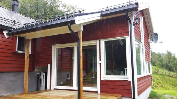 En rød hytte med liten terrasse med balkong dører og vindu som er vendt ut mot en liten veranda 